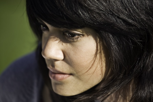 Environmental portrait of a young woman in profile, warm light against green