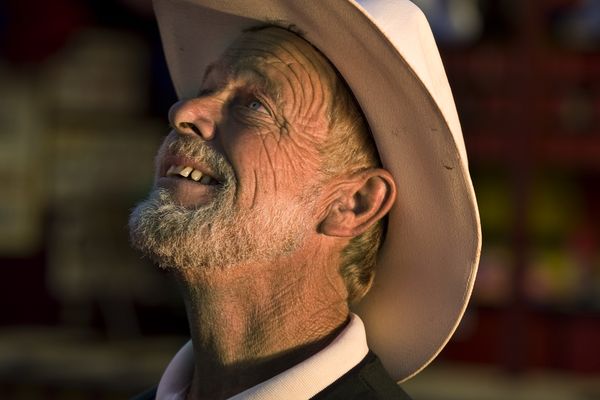 A weathered rancher in a cream cowboy hat, face turned to the sky in golden evening light
